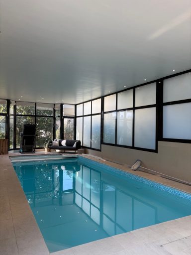 Piscine intérieure avec murs vitrés et mobilier moderne autour.
